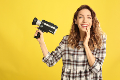 Beautiful young woman with vintage video camera on yellow background