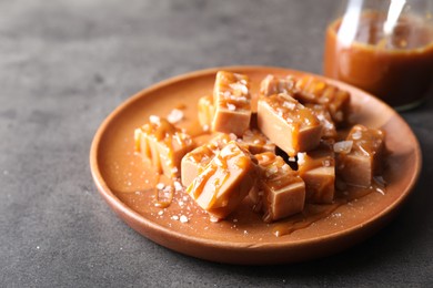 Photo of Plate with tasty candies, caramel sauce and salt on grey table, closeup