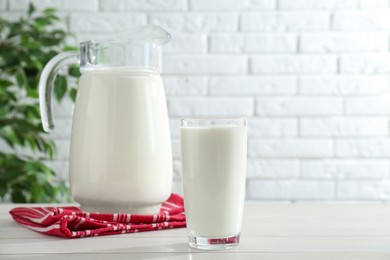 Photo of Jug and glass of fresh milk on white wooden table, space for text