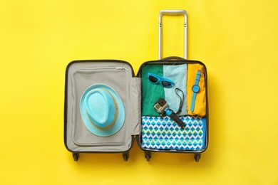 Photo of Open suitcase with summer clothes and accessories on color background, top view