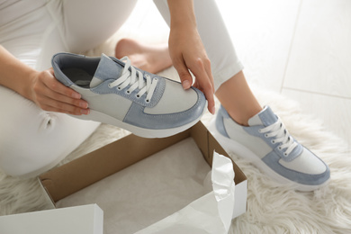 Photo of Woman measuring new stylish sneakers indoors, closeup