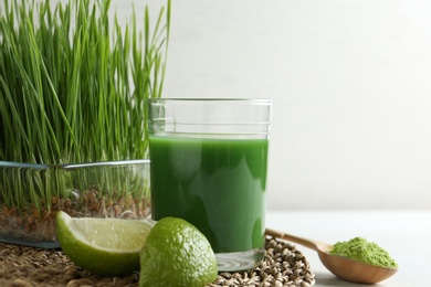 Photo of Composition with glass of wheat grass juice and lime on table against light background