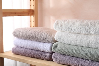 Photo of Stacked soft towels on wooden shelf indoors