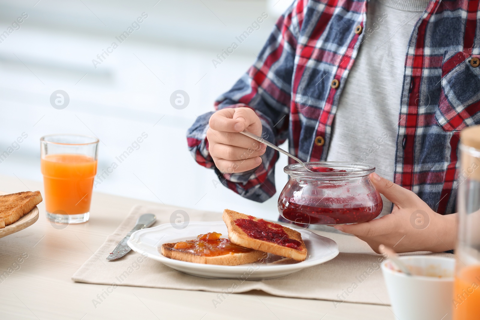 Photo of Cute little boy spreading jam onto tasty toasted bread at table