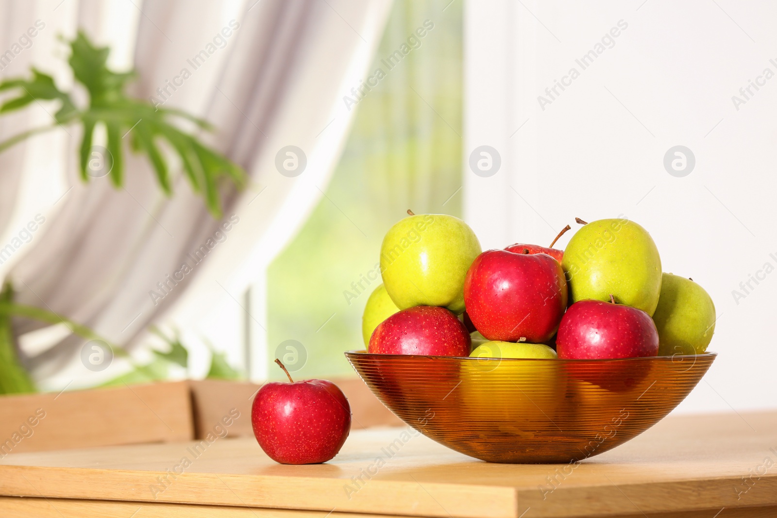 Photo of Bowl with different sweet apples on table in room, space for text