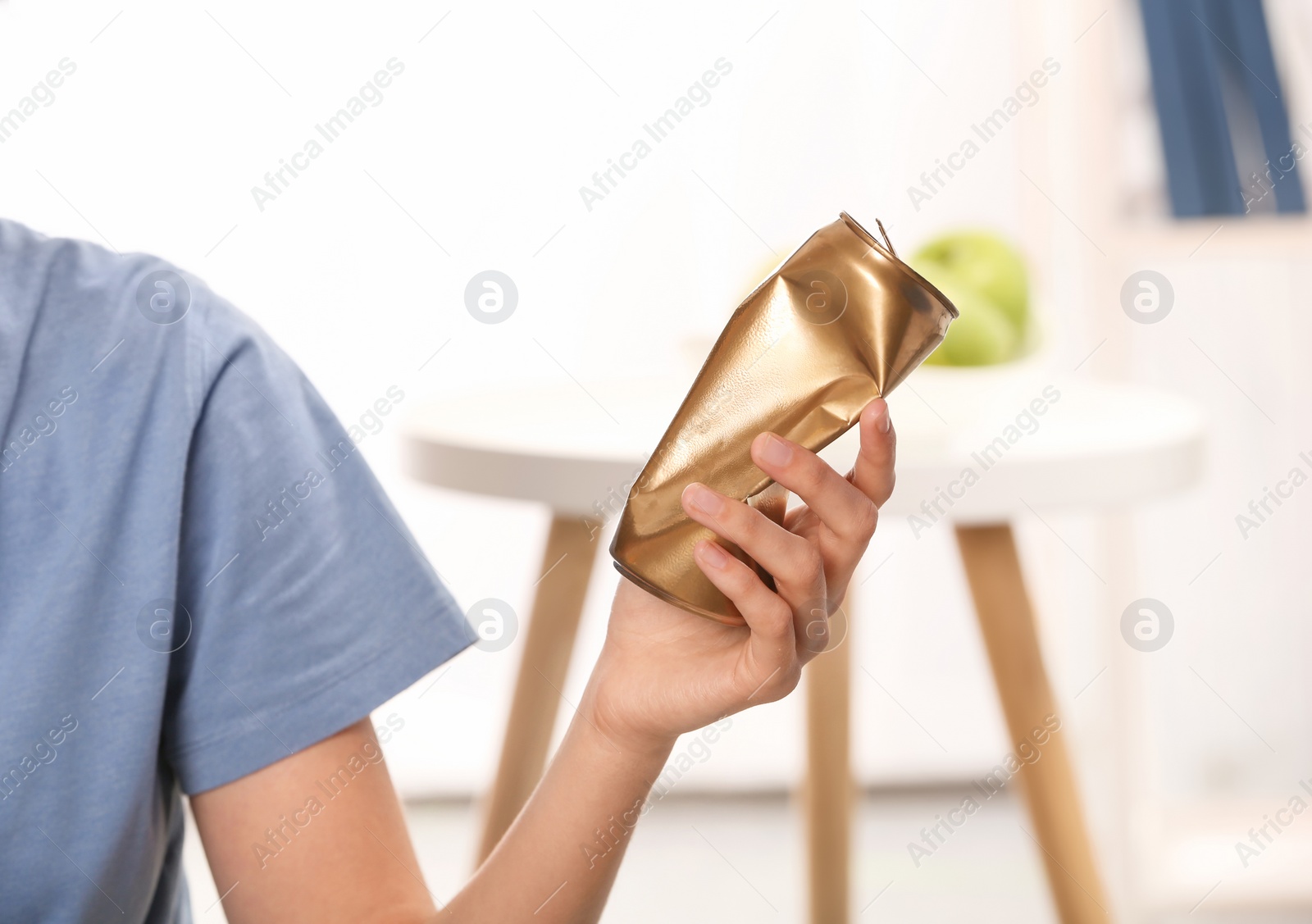 Photo of Woman holding crumpled aluminum can on blurred background. Metal waste recycling