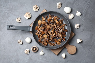 Frying pan with mushrooms on grey background, flat lay