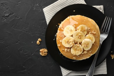 Photo of Delicious pancakes with bananas, walnuts and honey on dark textured table, top view. Space for text