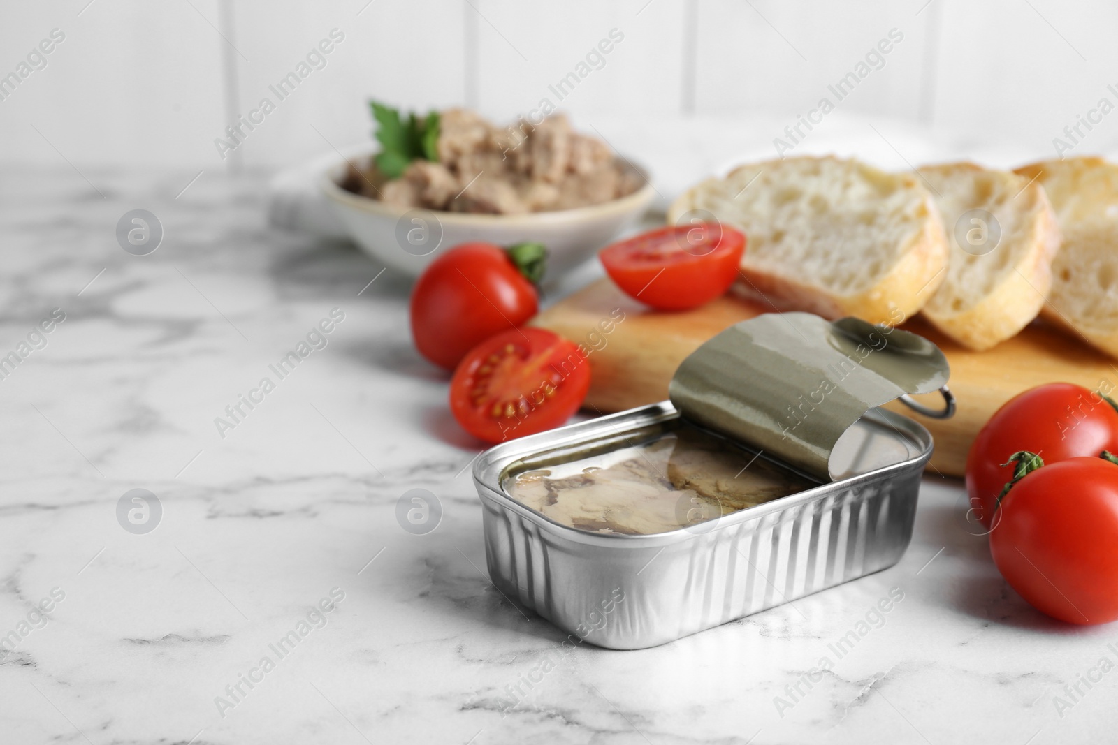 Photo of Open tin can of tasty cod liver and different products on white marble table. Space for text
