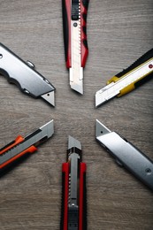 Many different utility knives on wooden table, flat lay