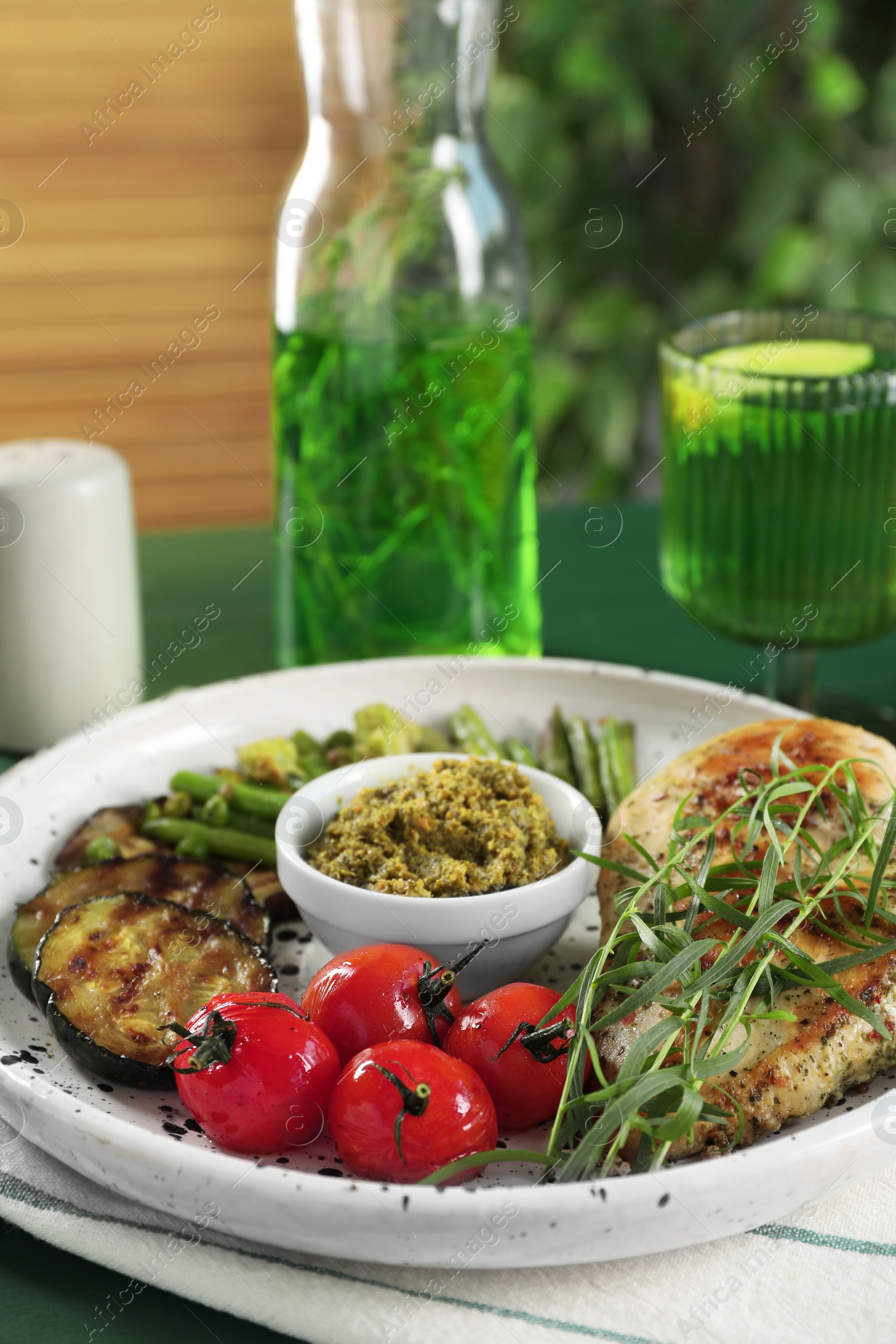 Photo of Tasty chicken, vegetables with tarragon and pesto sauce on green table, closeup