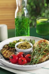Photo of Tasty chicken, vegetables with tarragon and pesto sauce on green table, closeup