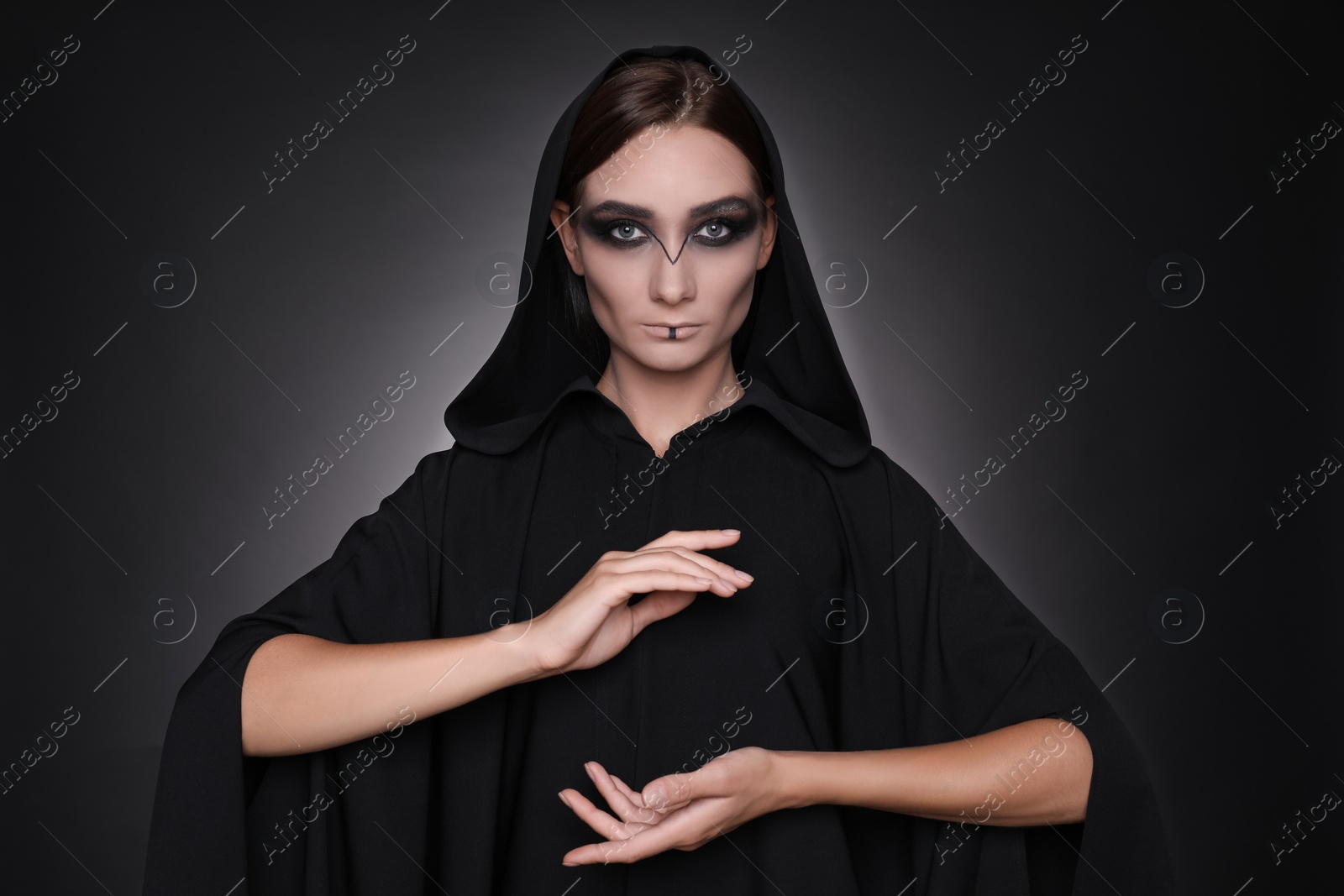 Photo of Mysterious witch in mantle with hood on dark background