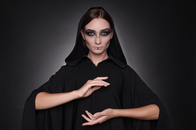 Mysterious witch in mantle with hood on dark background