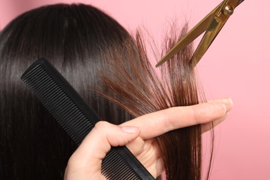 Hairdresser cutting client's hair with scissors on pink background, closeup