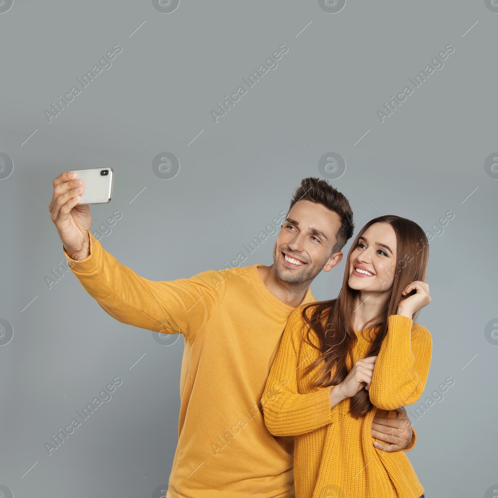 Photo of Happy young couple in warm clothes taking selfie on grey background. Winter season