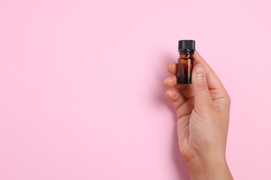 Photo of Woman with bottle of essential oil on pink background, closeup. Space for text