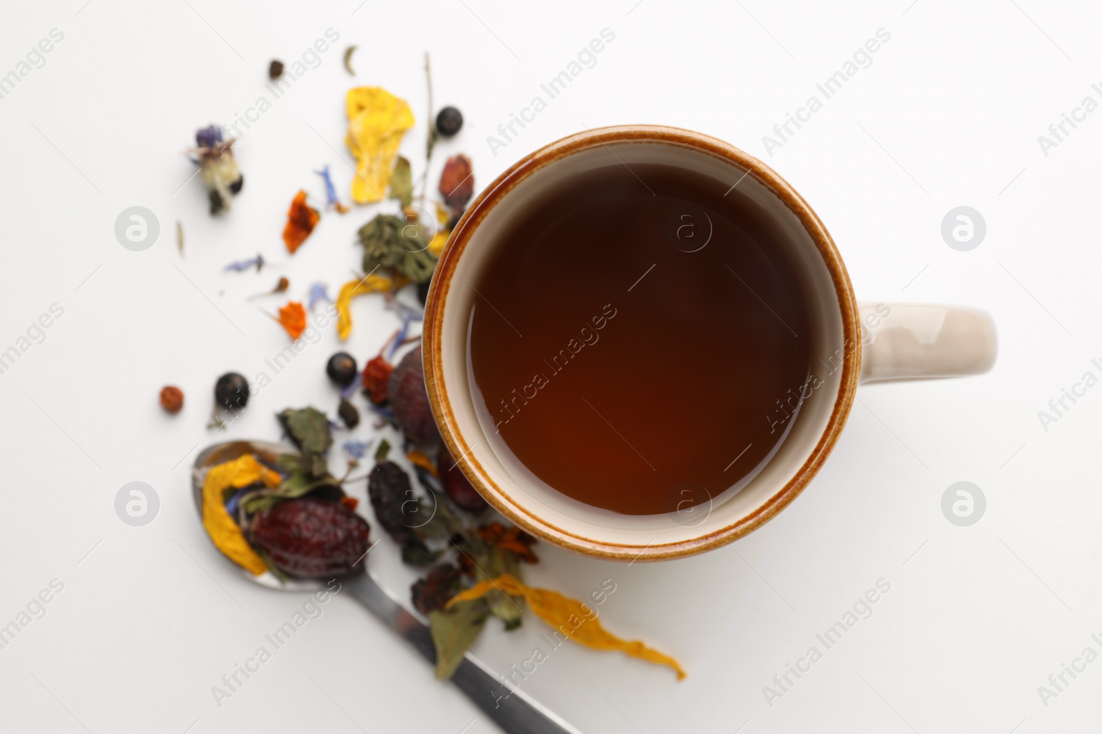 Photo of Cup of freshly brewed tea, dried herbs and spoon on white background, flat lay