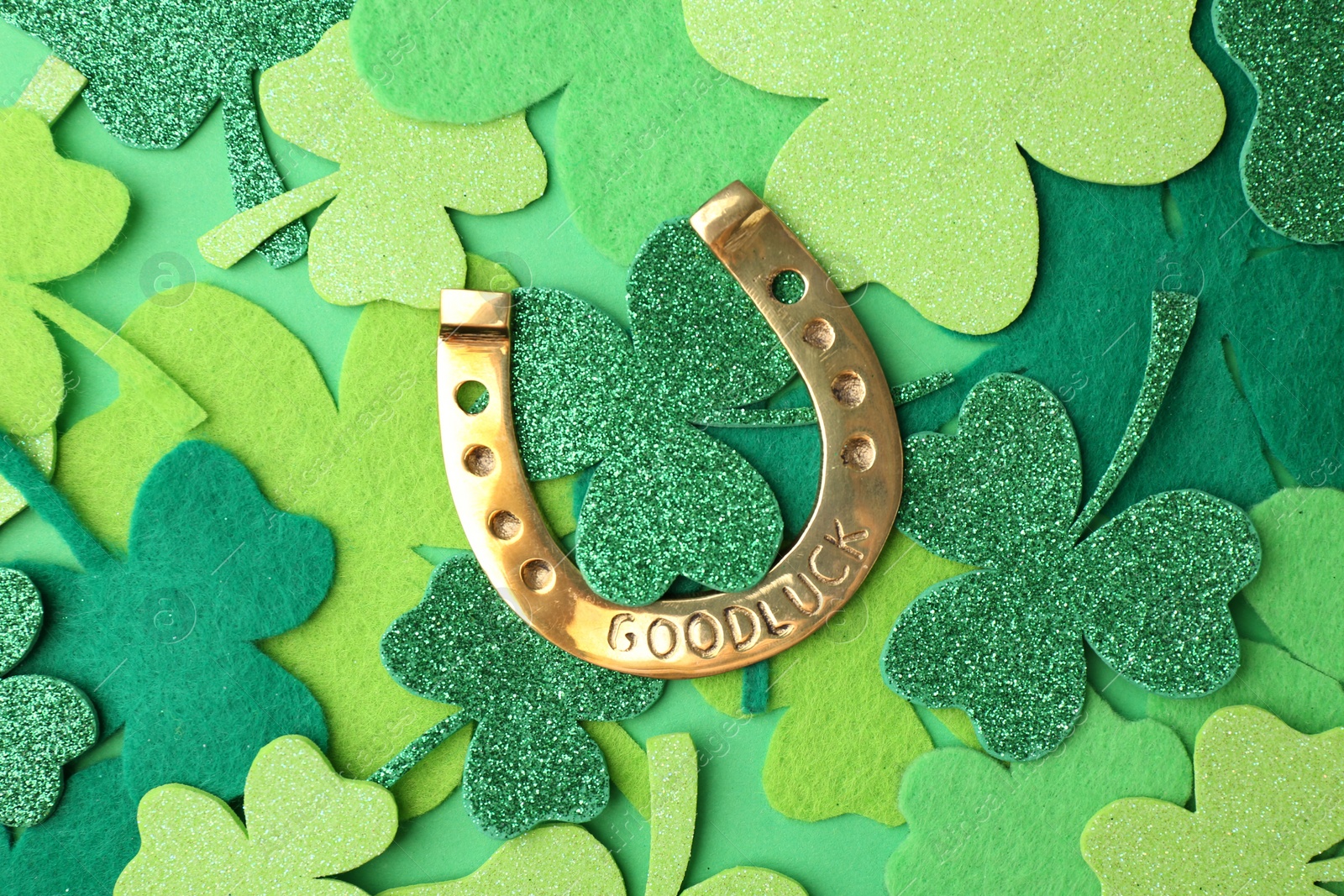 Photo of St. Patrick's day. Golden horseshoe and decorative clover leaves on green background, flat lay