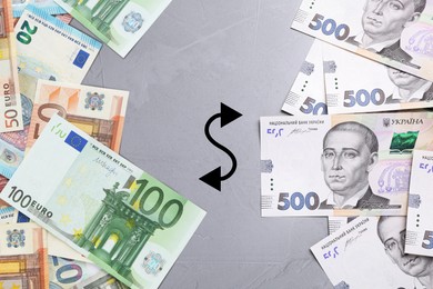 Image of Currency exchange. Double-headed wave arrow between hryvnias and euro banknotes on grey background, flat lay
