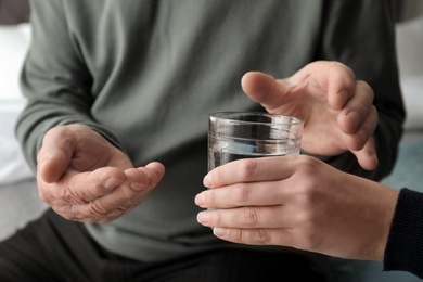 Young woman giving water to senior man with pills, closeup
