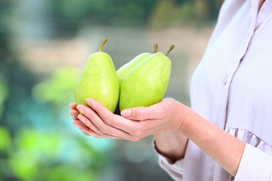 Photo of Woman holding fresh ripe pears against blurred background, closeup
