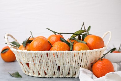 Photo of Basket with fresh ripe tangerines and leaves on grey table, closeup