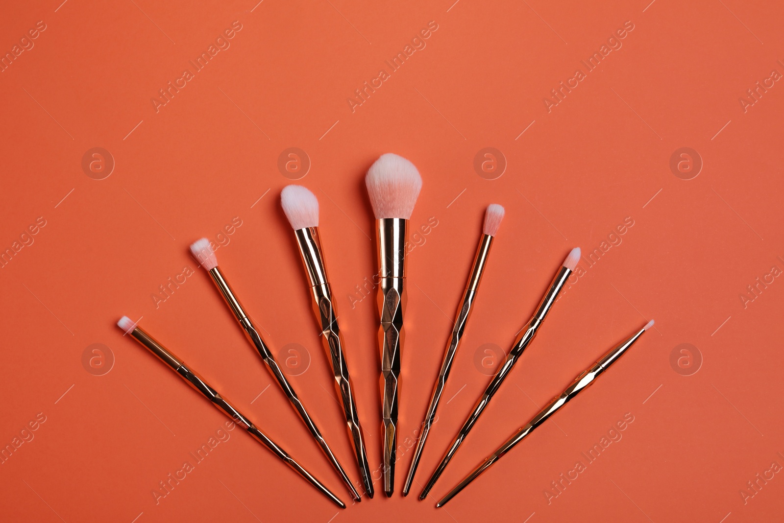 Photo of Set of cosmetics brushes on coral background, flat lay