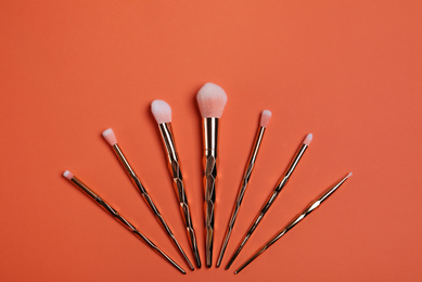 Photo of Set of cosmetics brushes on coral background, flat lay