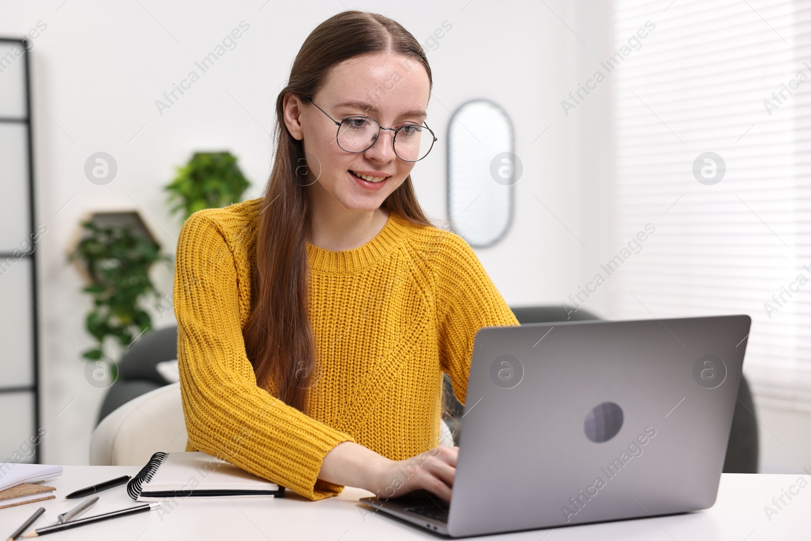 Photo of E-learning. Young woman using laptop during online lesson at white table indoors