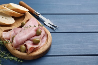 Photo of Slices of delicious ham with olives and baguette served on blue wooden table. Space for text