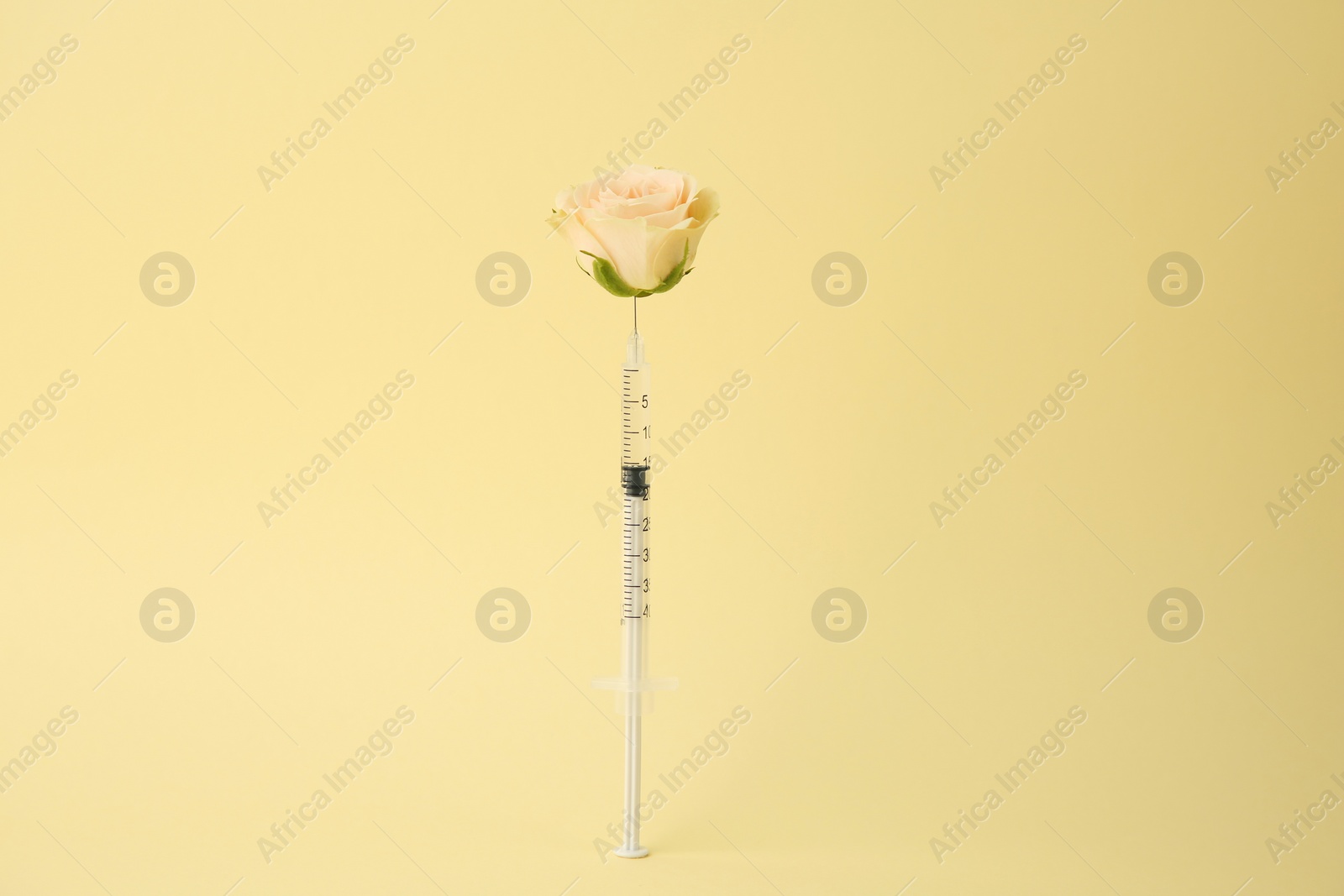 Photo of Medical syringe and rose flower on pale yellow background