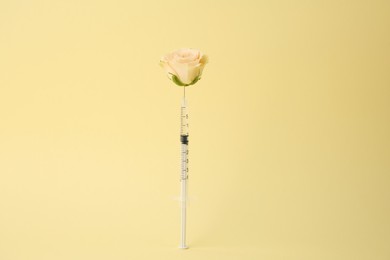 Medical syringe and rose flower on pale yellow background