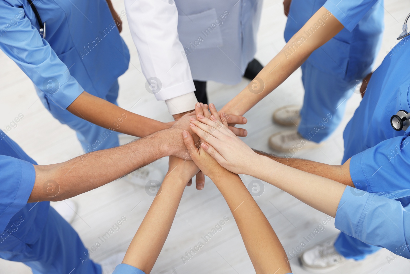 Photo of Doctor and interns stacking hands together indoors, closeup