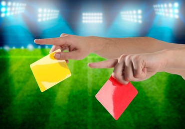 Referee holding red and yellow cards at stadium, closeup