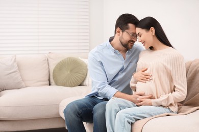 Photo of Happy pregnant woman with her husband on sofa at home, space for text