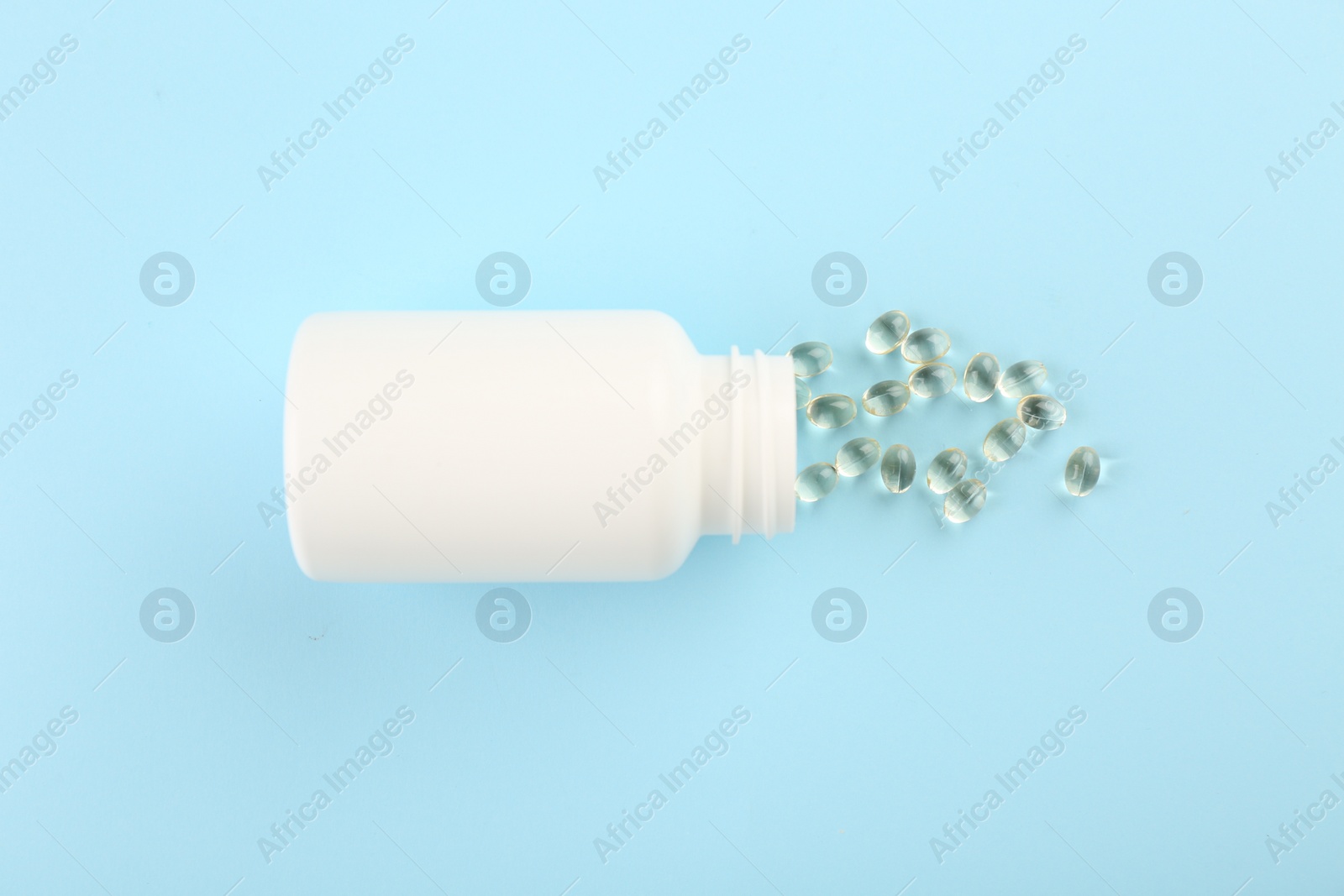 Photo of Bottle and vitamin capsules on light blue background, top view