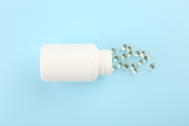 Photo of Bottle and vitamin capsules on light blue background, top view