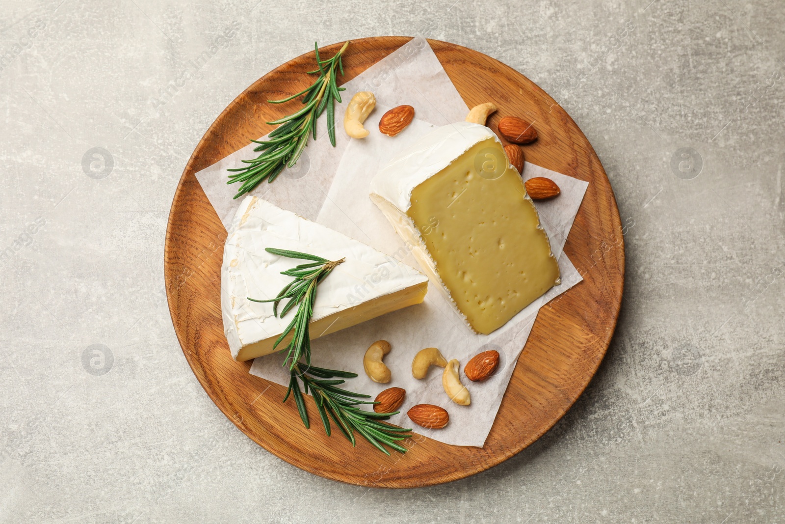 Photo of Plate with pieces of tasty camembert cheese, nuts and rosemary on grey textured table, top view