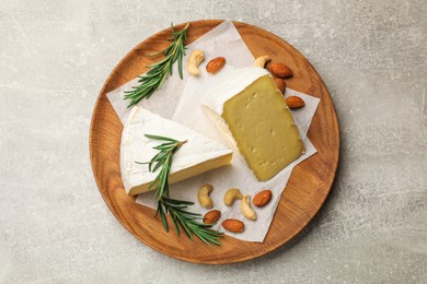 Photo of Plate with pieces of tasty camembert cheese, nuts and rosemary on grey textured table, top view