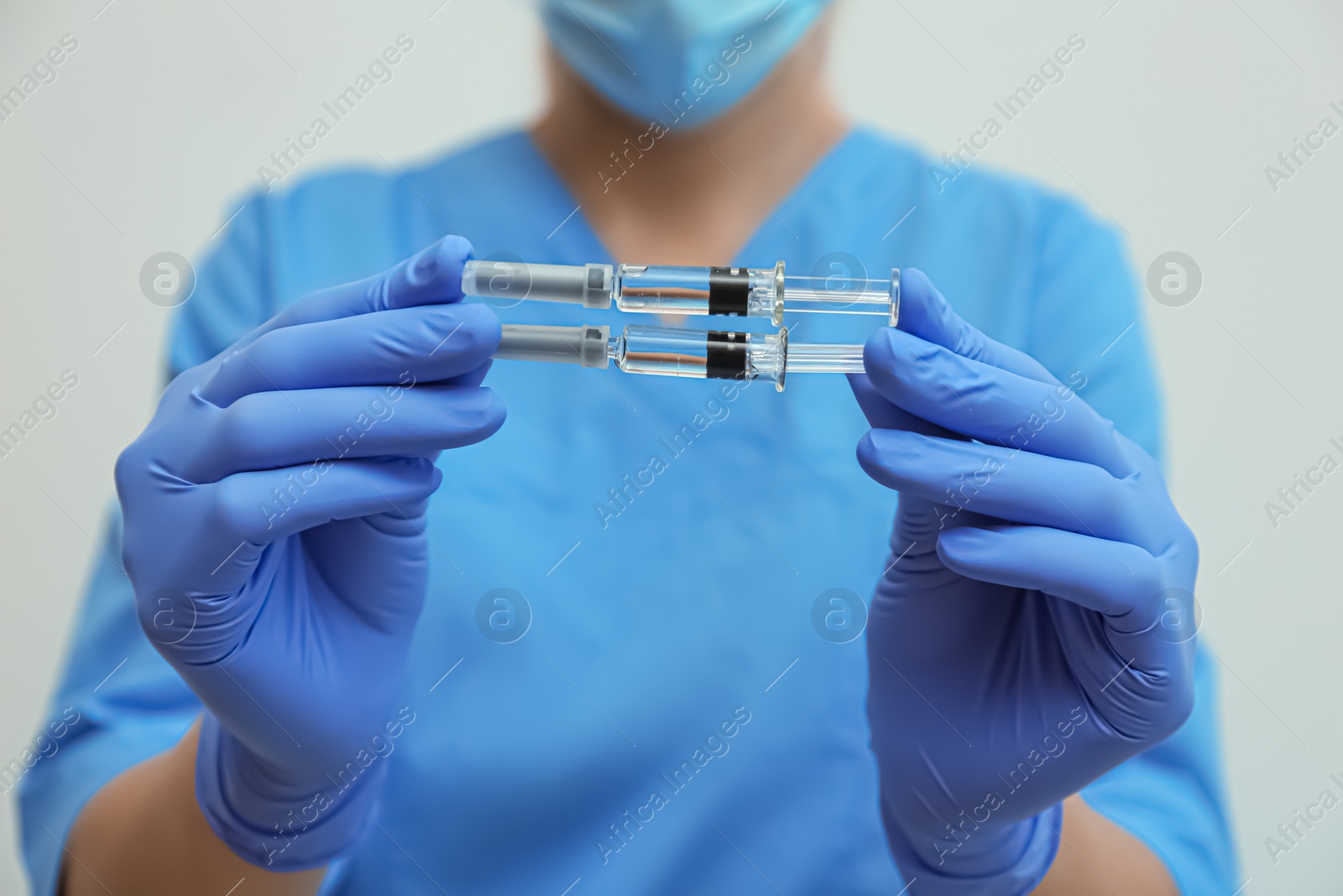 Photo of Doctor holding syringes with COVID-19 vaccine on light background, closeup