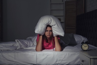 Photo of Young woman covering head with pillow in bed at home. Sleep disorder