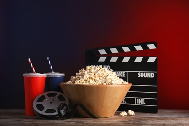 Photo of Composition with popcorn, cinema clapperboard and film reel on table against color background