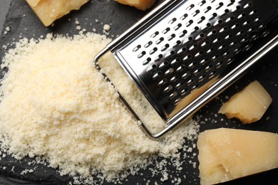 Photo of Pile of grated parmesan cheese and grater on black table, flat lay