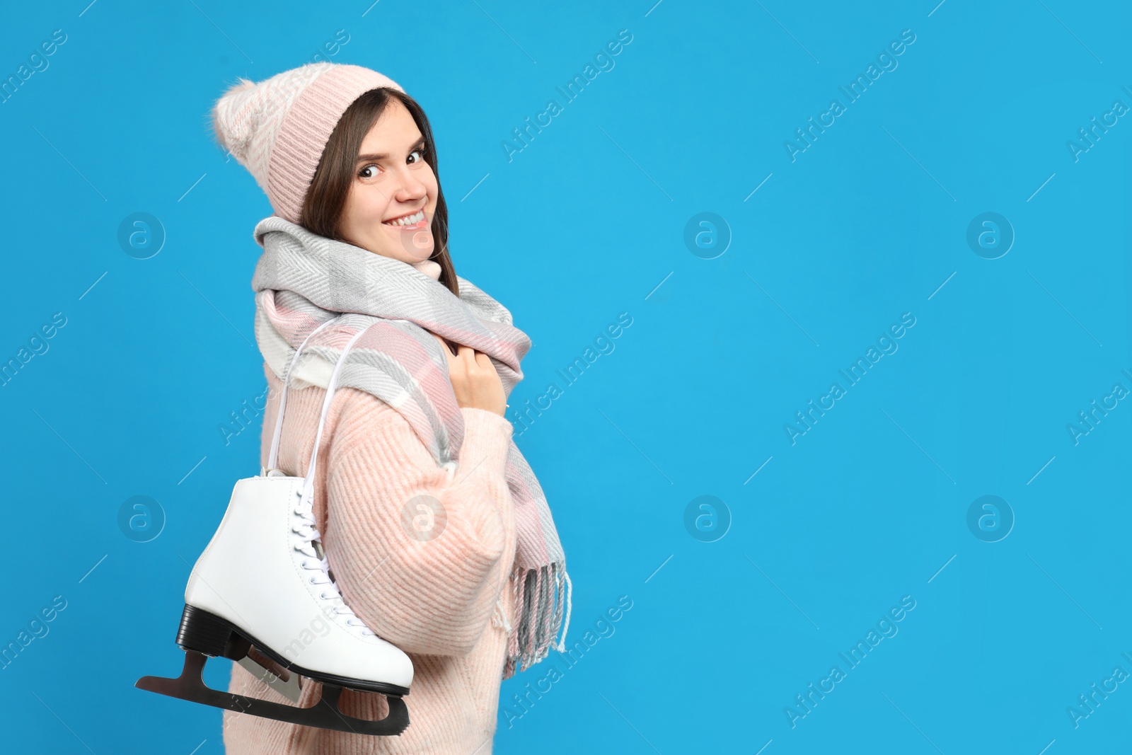 Photo of Happy woman with ice skates on light blue background. Space for text