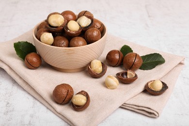 Photo of Bowl with organic Macadamia nuts and green leaves on white textured table