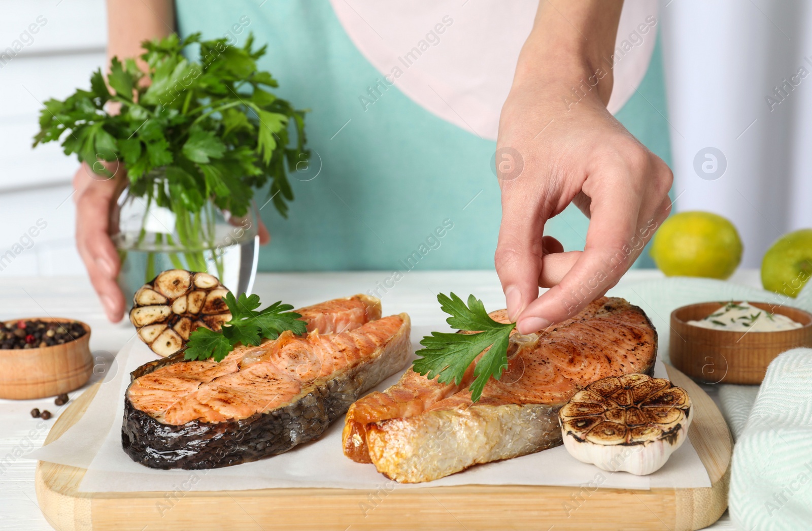 Photo of Woman adding parsley to cooked red fish on white wooden table, closeup