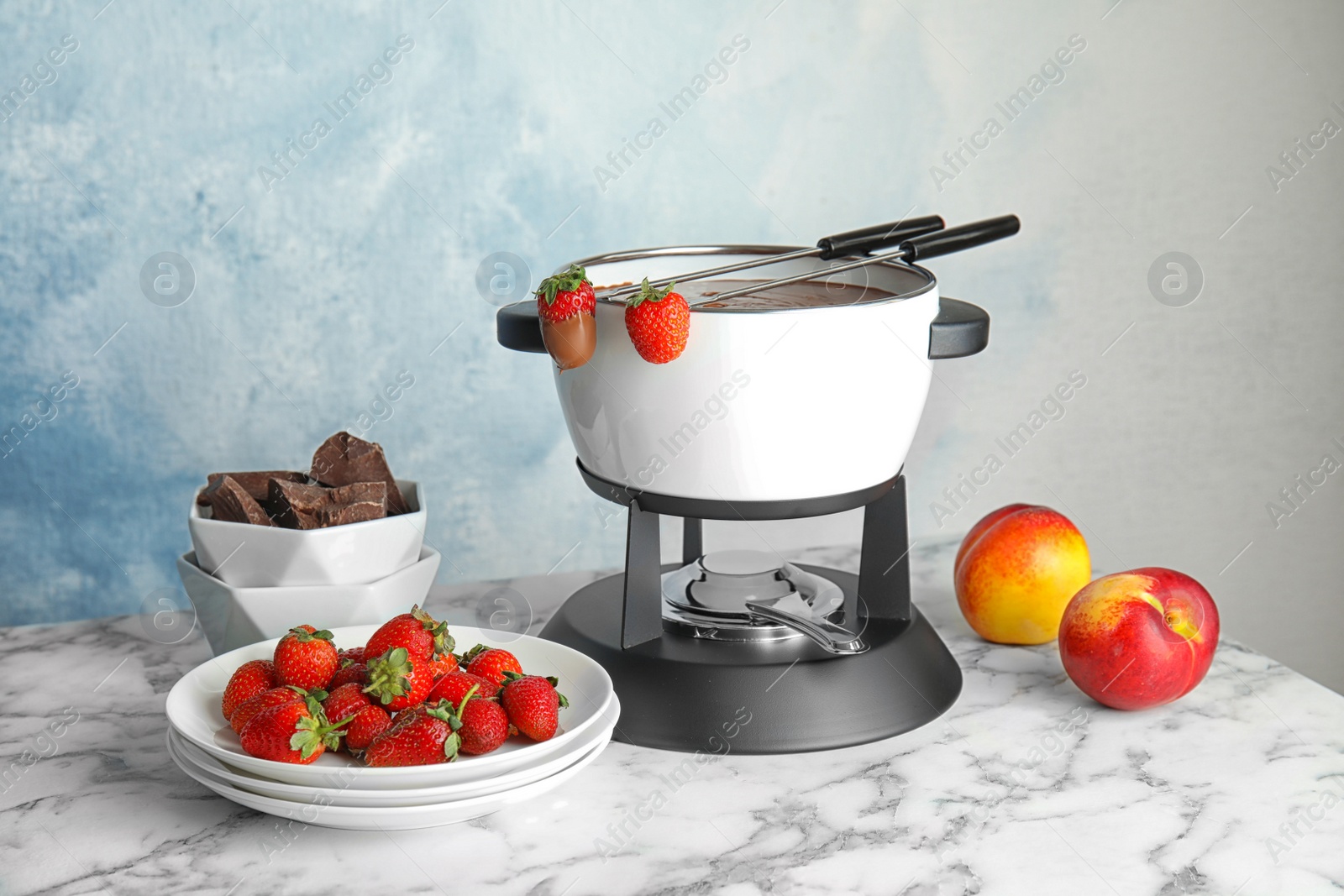 Photo of Chocolate fondue in pot and fresh fruits on marble table