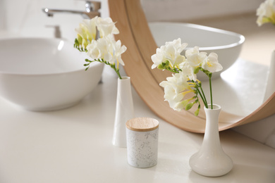 Photo of Beautiful white freesia flowers on countertop in bathroom