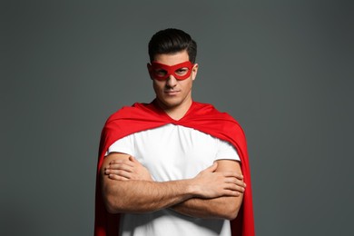 Man wearing superhero cape and mask on grey background